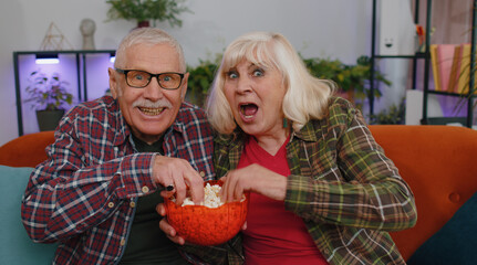 Senior elderly family couple grandparents man woman watching interesting television movie,...