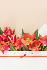 Beautiful bouquet of tulips in a white gift paper bag on a pink background with copy space. Holiday flower composition with red tulips and congratulation card with empty space. Vertical composition