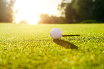 Golf ball on the green grass near hole on a golf course at sunset