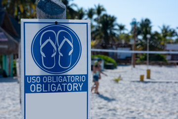 Sign in Spanish and English at the beach "obligatory". Mandatory to use flip-flops on the beach