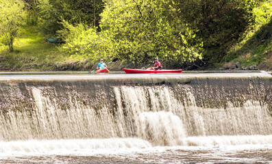 Elora, Ontario, Canada - 05 15 2022: Rowers in bright red kayaks beside waterfalls of the Grand...