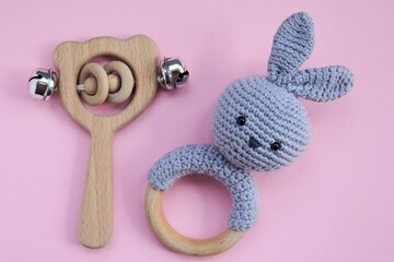 Baby wooden rattle and knitted wooden toy in the form of a rabbit on pink background. Concept of baby wooden toys. 