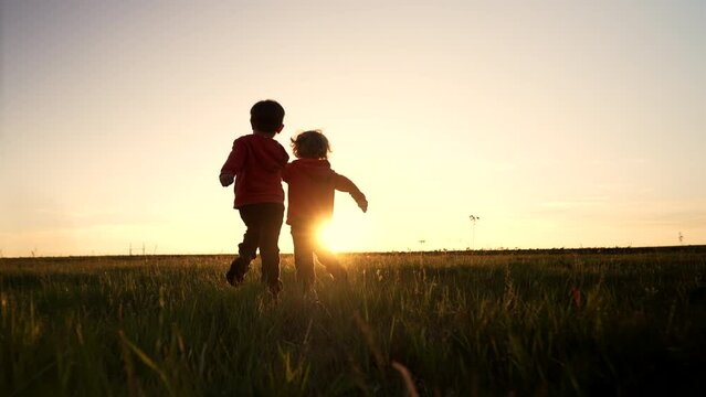 Silhouette of two little boys running together to the sun on open area field , friends holding hands. Children is our future, kids playing. Nature background. Happy childhood.