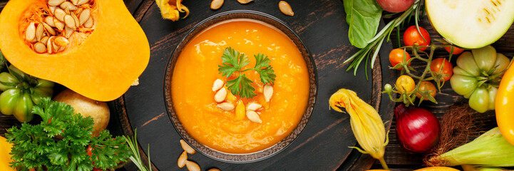 Pumpkin soup and various vegetables on a dark background. Top view.