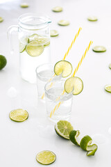  On a white table is a glass jug of lime lemonade, next to it are two glasses filled with lemonade and lots of limes. - 508820409