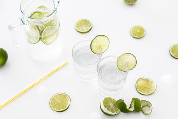 On a white table is a glass jug of lime lemonade, next to it are two glasses filled with lemonade...