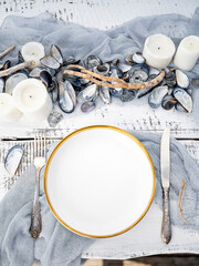 Luxury table setting in marine style with candles, mussels shells and grey-blue toned napkins. Table served for engagement, wedding, romantic dinner or festive event. Outdoor catering or dining.