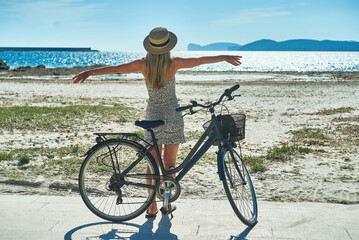 Fototapeta premium Carefree woman with bike riding on sand beach having fun, on the seaside promenade on a summer day.
