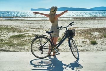 Carefree woman with bike riding on sand beach having fun, on the seaside promenade on a summer day.