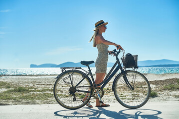 Carefree woman with bike riding on sand beach having fun, on the seaside promenade on a summer day.