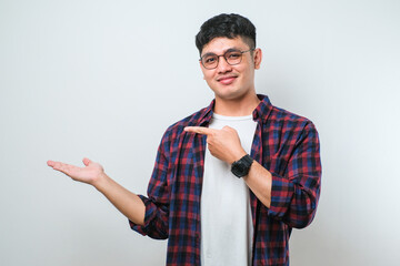 Young handsome asian man pointing with hand finger to the side looking at the camera.