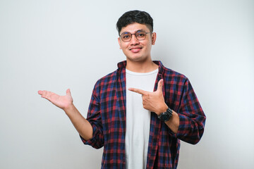 Young handsome asian man pointing with hand finger to the side looking at the camera.