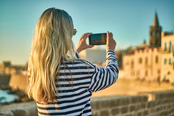 Woman traveler tourist using smartphone, taking photo of sea view at sunset in summer day. Enjoying European, Famous popular touristic place in world.
