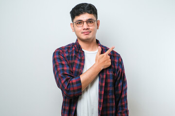 Young handsome asian man pointing with hand finger to the side looking at the camera.
