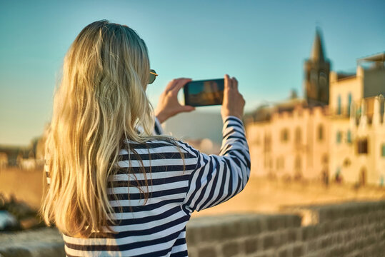 Woman traveler tourist using smartphone, taking photo of sea view at sunset in summer day. Enjoying European, Famous popular touristic place in world.
