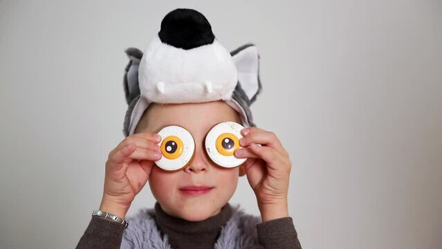 a close-up of funny boy kid in a wolf costume playing with eye-looking halloween cookies. Studio shot