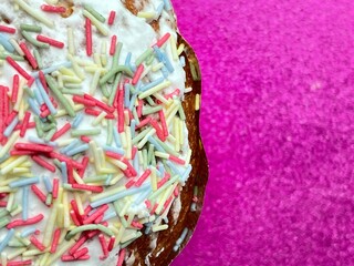 Top view cropped close up of delicious paska easter cake with sprinkles and frosting, pink glitter background