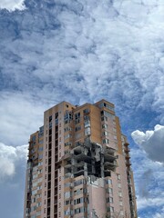 Low angle shot of a residentiol building damaged by rocket missile in the city of war, dramatic sky on background