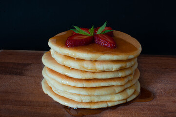 Pancakes with fresh strawberries, maple syrup and mint on wooden plate. Isolated on dark, selective focus.