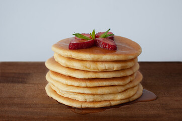 Pile of tasty homemade pancakes with maple syrup, strawberries and mint on top. Isolated on white background and selective focus.