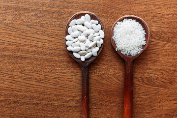 White rice and white beans on wooden kitchen spoons. Brown, wooden background.