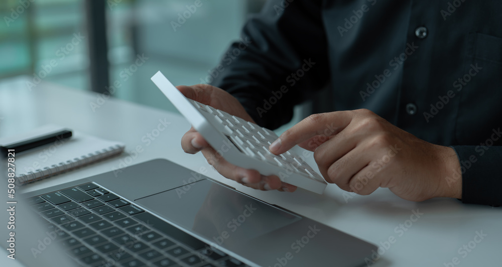 Poster accounting businessman working at his desk, using a laptop computer and a calculator to analyze data