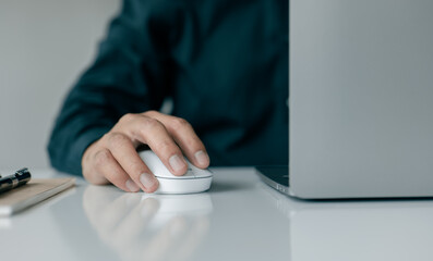 A man hand holds a computer mouse and types on a laptop keyboard.