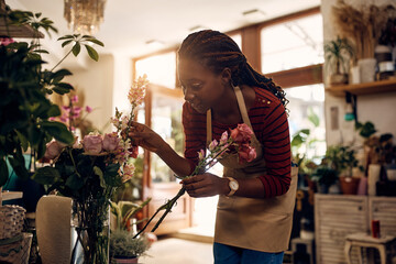 Creative black florist arranging flowers while working at her flower shop.