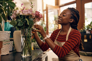 Young black woman arranging flowers while working at flower shop.