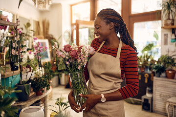 Happy black florist with fresh flower arrangement at her shop.