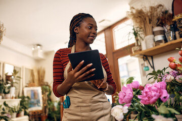 Young black female florist uses digital tablet while working at flower shop.