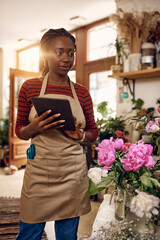 Young African American woman works on touchpad at flower shop.