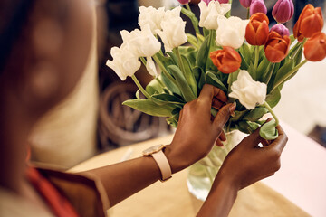Close up of woman arranging tulips in vase while working at flower shop.