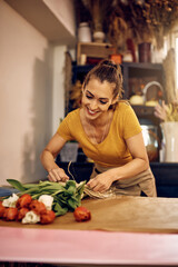 Young happy florist making bouquet of tulips at her flower shop.