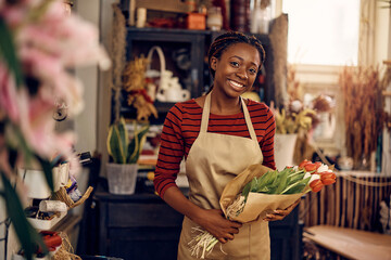 Happy African American florist holding bouquet of tulips and looking at camera. - obrazy, fototapety, plakaty