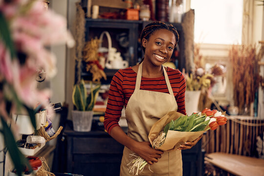 Happy African American florist holding bouquet of tulips and looking at camera. - Powered by Adobe