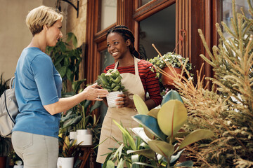 Happy African American flower shop owner and her customer talking about potted flowers.