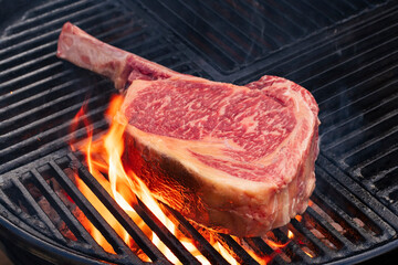 Barbecue dry aged Wagyu tomahawk steak offered as close-up on a charcoal grill with fire and smoke