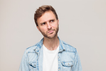 Young hipster male with stubble in a white t-shirt and light blue denim shirt. Emotion - thinks...