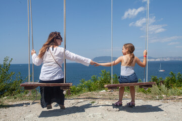 Mother and daughter together on swings on sea beach. Happy family concept