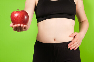 A woman on a green background holds a red apple in her hand. The concept of proper nutrition,...