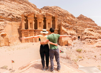 A young couple standing with open arms looking at the monastery of petra - Jordan - travel
