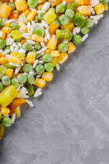 Mixed frozen vegetables with rice on a gray background. Frozen vegetables retaining all nutrients: green peas, corn, bell pepper. Healthy frozen food concept. Top view. Copy space