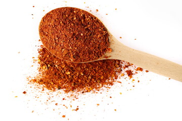Spicy chili pepper flakes, crushed, milled red paprika pile in wooden spoon isolated on white, top...