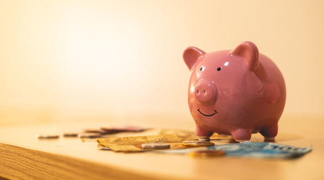 Um cofrinho com algumas c&eacute;dulas e moedas do Real Brasileiro, dinheiro do Brasil, sobre um m&oacute;vel de madeira em uma sala de uma casa. Conceitos de guardar dinheiro, poupan&ccedil;a e investimentos.