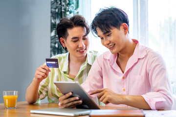 Portrait of young gay couple, lgbt man holding credit card enjoy shopping online with laptop at home. LGBT and love concept.