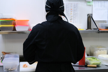 a cook in a black jacket stands with his back in a kitchen