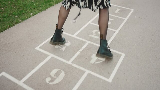 Close-up of young woman hopscotching on city playground. Closeup of the legs of a girl jumping on the drawn cells on the pavement.