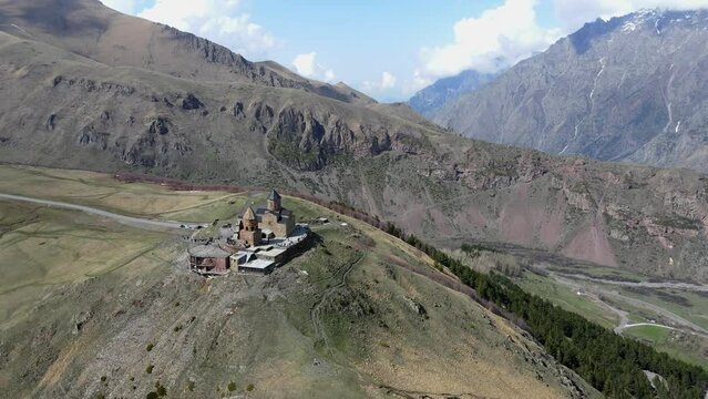 Camera drone flies forward over Holy Trinity Church (Gergeti Trinity Church) near the village of Stepantsminda in Georgia. Mount Kazbek is seen in the upper right.