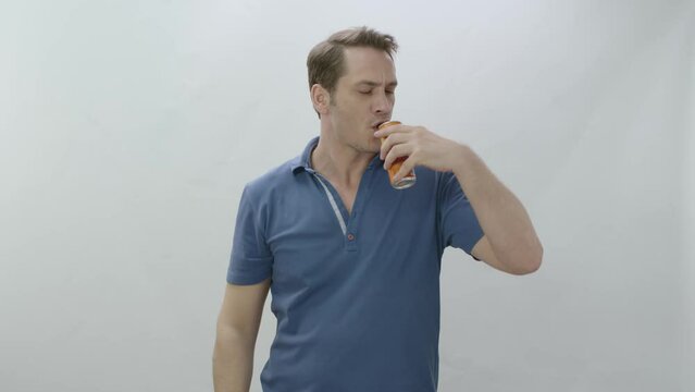 Young man drinks fizzy Fanta beverage from metal bottle. Slow motion video. The young man is drinking Fanta and is happy to cool off. Slow motion video. Indoor studio isolated on white background.